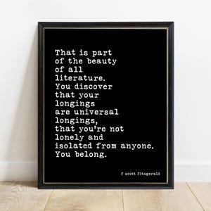 May include: A black framed wall art print featuring white typewriter-style text that reads: That is part of the beauty of all literature. You discover that your longings are universal longings, that you're not lonely and isolated from anyone. You belong. f scott fitzgerald.