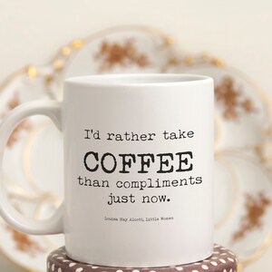 May include: White ceramic coffee mug with black text that reads "I'd rather take COFFEE than compliments just now. Louisa May Alcott, Little Women".