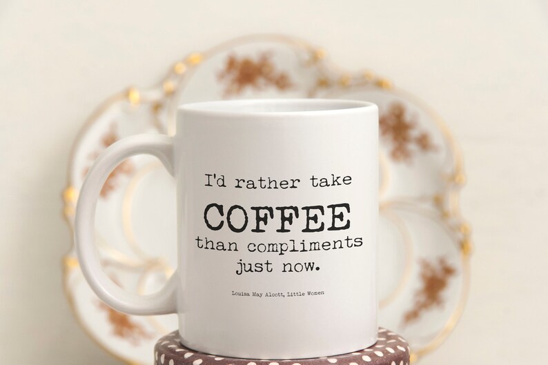 May include: White ceramic coffee mug with black text that reads "I'd rather take COFFEE than compliments just now. Louisa May Alcott, Little Women".