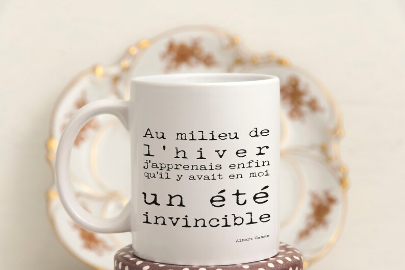 May include: White ceramic mug with a black quote in French: "Au milieu de l'hiver j'apprenais enfin qu'il y avait en moi un &eacute;t&eacute; invincible."  The quote is attributed to Albert Camus.