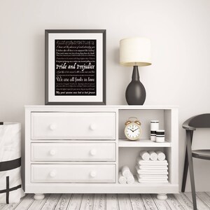 May include: A black and white framed print with a white background and black text. The text is a quote from the novel "Pride and Prejudice" by Jane Austen. The print is sitting on a white dresser with a black lamp and a gold alarm clock.