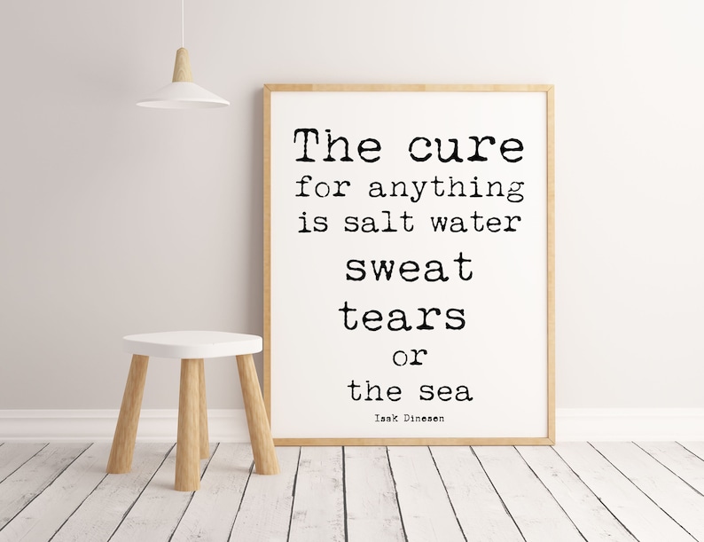 Pu&ograve; includere: Stampa incorniciata con la citazione "The cure for anything is salt water sweat tears or the sea" in testo nero su sfondo bianco. La cornice &egrave; marrone chiaro. Un piccolo sgabello bianco con gambe in legno &egrave; di fronte alla stampa.