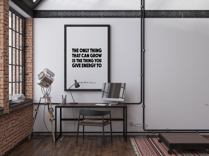 May include: An interior shot of a modern office space with a framed print that reads "THE ONLY THING THAT CAN GROW IS THE THING YOU GIVE ENERGY TO." The room features a desk, chair, and a vintage-style spotlight on a tripod.