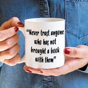 May include: White ceramic mug with a black quote that reads "Never trust anyone who has not brought a book with them."