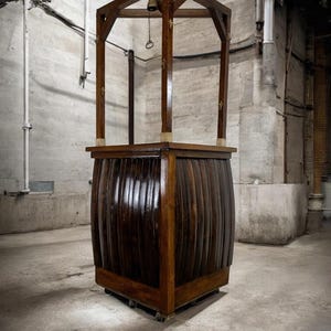 Può includere: Una struttura in legno scuro con una base a forma di botte e un tetto a punta. La struttura ha una piccola campana appesa al tetto ed è montata su ruote. Il legno ha una finitura lucida.