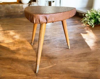 May include: A brown leather-covered three-legged stool with wooden legs.