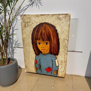 May include: A vintage painting of a young child with brown hair and large brown eyes. The child wears a blue shirt with colorful patches. The background has a textured, off-white appearance. The artwork is displayed on a tiled floor.