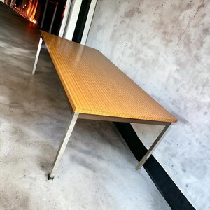 Könnte beinhalten: Ein rechteckiger Holztisch mit hellbrauner Holzmaserung. Der Tisch hat eine dunkelbraune Umrandung und wird von vier silbernen Metallbeinen getragen. Der Tisch ist etwa 244 cm lang.