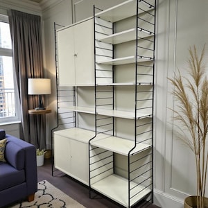 May include: A contemporary shelving unit featuring a black metal frame and white shelves and cabinets. The unit includes multiple shelves and two cabinets with doors. The design is minimalist and functional, ideal for storage and display.