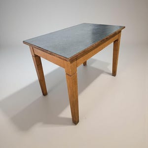 May include: A rectangular wooden table with a gray top. The table has four angled legs and a light brown finish. The tabletop appears to be made of a dark gray material. The table is approximately 30 inches long.