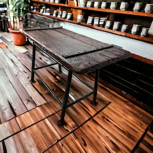 Op de afbeelding: Een rustieke, donkerbruine houten tafel met een metalen plaat en donkergroene metalen poten. De tafel staat op een houten vloer met een natuurlijk houtnerfpatroon. De tafel is ongeveer 91 cm lang en 61 cm breed.