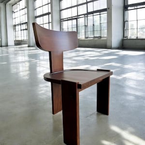 May include: A dark brown wooden chair with a unique design. The chair has a curved back and a wide, flat seat. The legs are straight and sturdy, and the chair is made of solid wood.