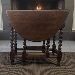 Può includere: Un tavolo antico marrone scuro con piano a ribalta a semicerchio. Il tavolo presenta gambe a spirale intagliate e un ripiano inferiore. Il tavolo è in legno ed è posto su un tappeto a righe. Misura circa 76 cm di altezza.