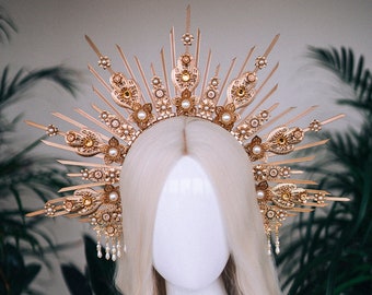 May include: A gold crown with pearl accents and a sunburst design. The crown is on a white mannequin head with blonde hair.