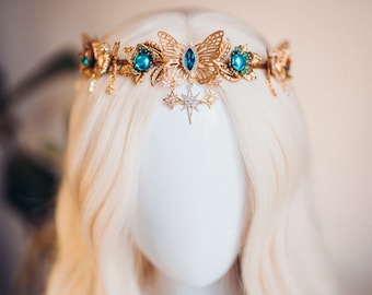 May include: Gold crown headband with a butterfly design, blue gems, and a star pendant. The crown is on a white mannequin head with blonde hair.