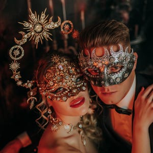 Peut inclure: Un couple portant des masques de bal masqué élaborés. Le masque de la femme est doré, avec un ornement de tête assorti. Le masque de l'homme est argenté et noir. Ils sont vêtus de tenues de soirée, sur fond sombre.