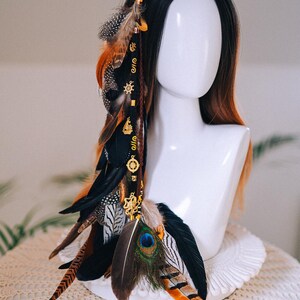 Puede incluir: Accesorio decorativo para el cabello con una combinaci&oacute;n de plumas en tonos negro, marr&oacute;n, naranja y azul pavo real. Adornado con abalorios y cuentas doradas, creando un estilo bohemio o festivalero. Para el cabello.