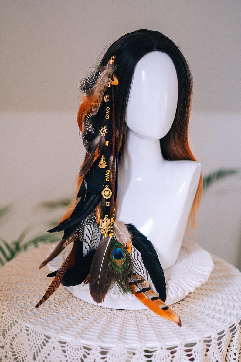Puede incluir: Accesorio decorativo para el cabello con una combinaci&oacute;n de plumas en tonos negro, marr&oacute;n, naranja y azul pavo real. Adornado con abalorios y cuentas doradas, creando un estilo bohemio o festivalero. Para el cabello.