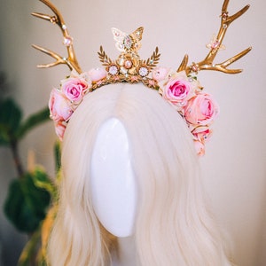 Puede incluir: Una diadema de asta de ciervo dorada con rosas rosas y un dije de mariposa. La diadema est&aacute; decorada con hojas doradas y pedrer&iacute;a.
