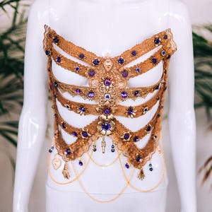May include: A gold-toned, beaded, and lace body chain with purple gemstones. The chain is layered and has a delicate, feminine design.