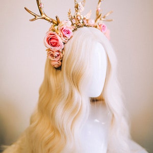 Puede incluir: Una diadema de asta de ciervo dorada adornada con rosas rosas y pedrer&iacute;a. La diadema se lleva en un maniqu&iacute; blanco con el pelo largo y rubio.