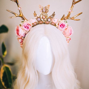 Puede incluir: Una diadema de asta de ciervo dorada con flores rosas y un dije de mariposa. La diadema est&aacute; decorada con perlas y pedrer&iacute;a.