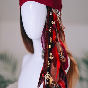 以下が含まれることがあります： ブルゴーニュ色のヘッドラップと長い編み込みヘアエクステンション。エクステンションは赤、茶色、黒の羽と金色のチャームで飾られています。チャームには、錨、コンパス、その他の航海をテーマにしたデザインが含まれています。