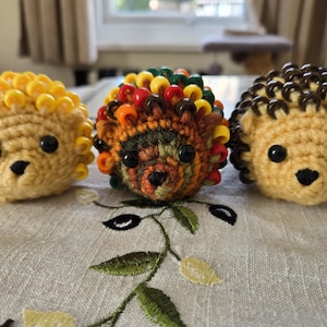 May include: Three crocheted hedgehogs with different coloured beads. The first hedgehog has yellow beads, the second has red, orange, yellow, and green beads, and the third has brown beads.
