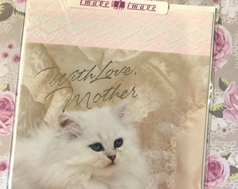 May include: A white kitten with blue eyes lies on a pink and white lace fabric. The text "With Love, Mother" is written in gold script above the kitten.