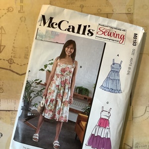 May include: McCall's sewing pattern M8193, size A5/F5 (6-24), featuring three different styles of dresses. The pattern includes simple instructions and multiple view options. The dresses are shown in a variety of colors and patterns, including floral, blue, and pink.
