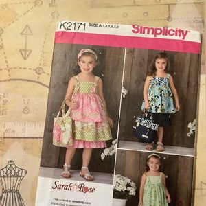 May include: A sewing pattern for a girl's dress with a tiered skirt. The pattern is from Simplicity and is called K2171. The pattern includes three different styles of dresses, all with a tiered skirt. The dresses are shown on three different girls, each wearing a different style of dress. The pattern is available in sizes 3-8.