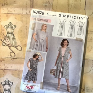 May include: A Simplicity sewing pattern for a dress, pattern number K8879, called "The Origami Dress". The pattern shows three different styles of the dress, with a model wearing each style. The pattern is for sizes XXS-XXL.