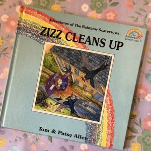 Op de afbeelding: Een blauw boek met een regenboogontwerp op de omslag. De titel is "Zizz Cleans Up" en het maakt deel uit van de serie "Adventures of The Rainbow Scarecrows". Het boek is van Tom & Patsy Allen.