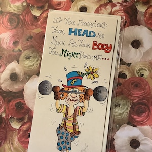 Peut inclure: Une carte de vœux humoristique avec un clown de dessin animé soulevant des poids. Le texte de la carte dit : « Si vous exerciez votre TÊTE autant que votre CORPS, vous pourriez devenir... » Le clown porte un chapeau coloré, des bretelles et un pantalon à pois. La carte est dans une pochette en plastique transparent.