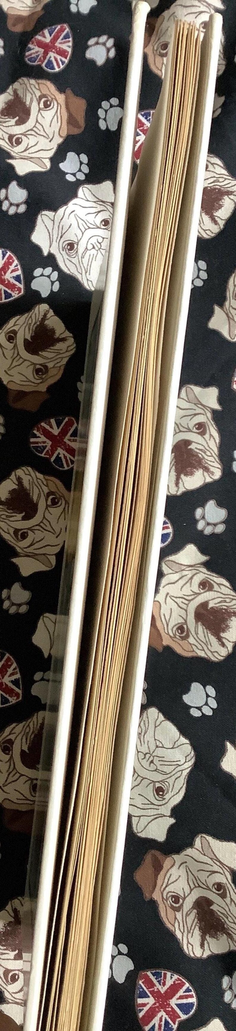 Puede incluir: Un &aacute;lbum de fotos abierto, con lomo blanco, mostrando las p&aacute;ginas. El fondo es una tela negra estampada con caras de bulldog, huellas de patas y emblemas de la Union Jack. El &aacute;lbum est&aacute; abierto.
