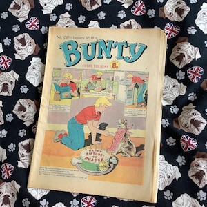 May include: A vintage "Bunty" comic book from January 20, 1979, featuring a colorful illustration of a birthday scene. The comic is set on a black fabric patterned with bulldog faces, paw prints, and Union Jack flags.