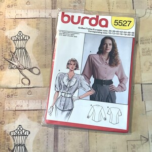 May include: A Burda sewing pattern for a blouse with raglan shoulders. The pattern number is 5527. The European sizes are 36-38-40-42-44-46-48. The corresponding sizes are 10-12-14-16-18-20-40.