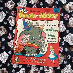 May include: A vintage comic book cover featuring Donald Duck and Mickey Mouse. The cover is red and white with a picture of Dumbo the elephant and the Aristocats. The text on the cover reads "Walt Disney's Donald and Mickey" and "This Week: The Aristokittens meet Dumbo The Flying Elephant!"