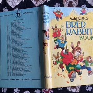 May include: Open vintage children's book titled "Brer Rabbit Book" by Enid Blyton. The cover features illustrations of rabbits in colorful clothing. The book is open, revealing a list of stories and the title page.