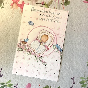 Tarjeta vintage rara de nacimiento de niña de los años 80: adorable bebé acurrucada en la cama, pájaros azules y un bonito diseño floral. Verso dulce en el interior.