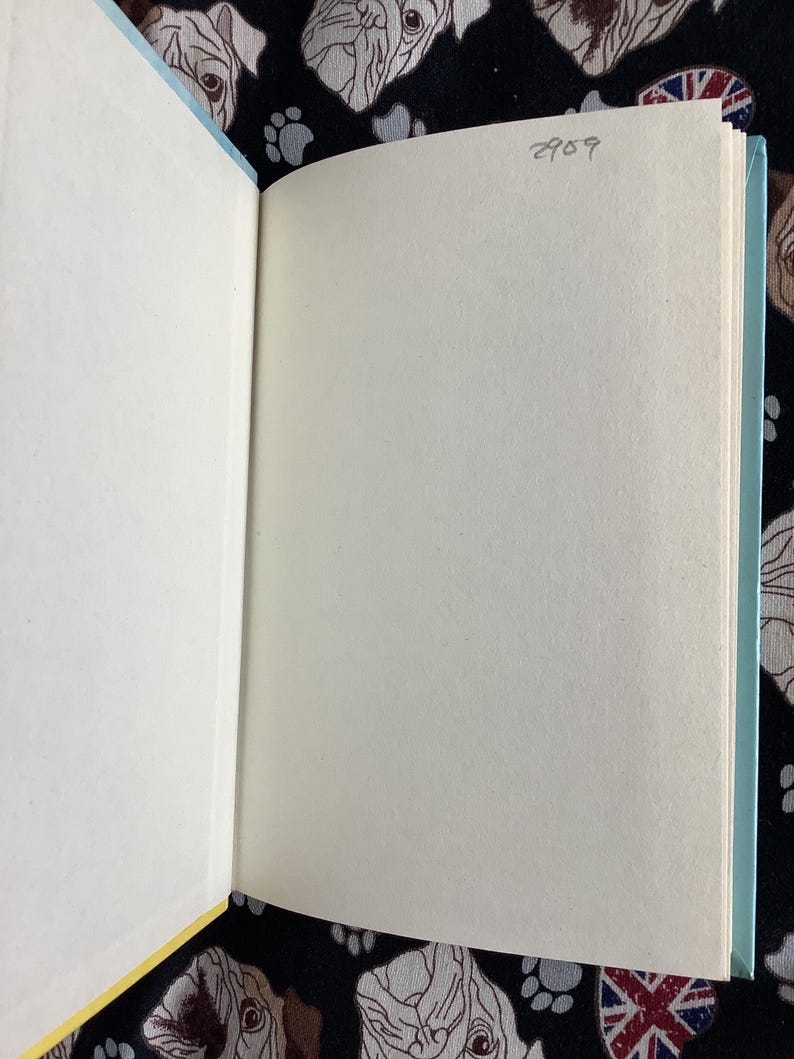 May include: Open book with blank pages. The book's spine is light blue, and the pages are off-white. The background is a black fabric with a pattern of dog faces and paw prints. The number "2909" is written in pencil on the top right page.