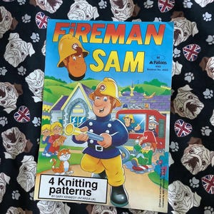 Może przedstawiać: Kolorowa książka zatytułowana "Fireman Sam" z ilustracjami strażaka z kreskówki i innych postaci. Na okładce znajduje się również tekst "4 Knitting patterns". Książka jest osadzona na czarnym tle z wzorem białych twarzy buldogów i flag Union Jack.
