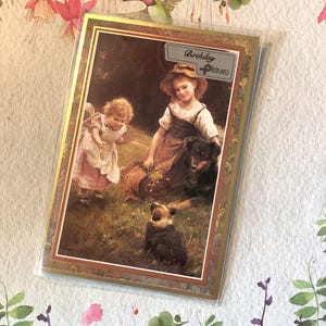 May include: A greeting card with a vintage illustration of two young girls, a large dog, and a puppy in a grassy field. The card has a gold border and the text "Birthday Picture".