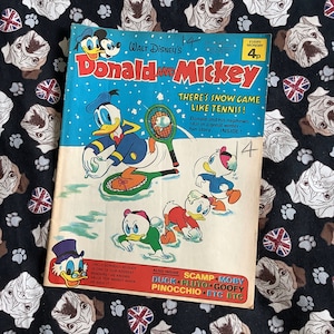 May include: A vintage comic book cover featuring Donald Duck and Mickey Mouse playing a snow game. The cover is blue and white with the title "Donald and Mickey" in red and black. The text "There's Snow Game Like Tennis!" is in black and white.