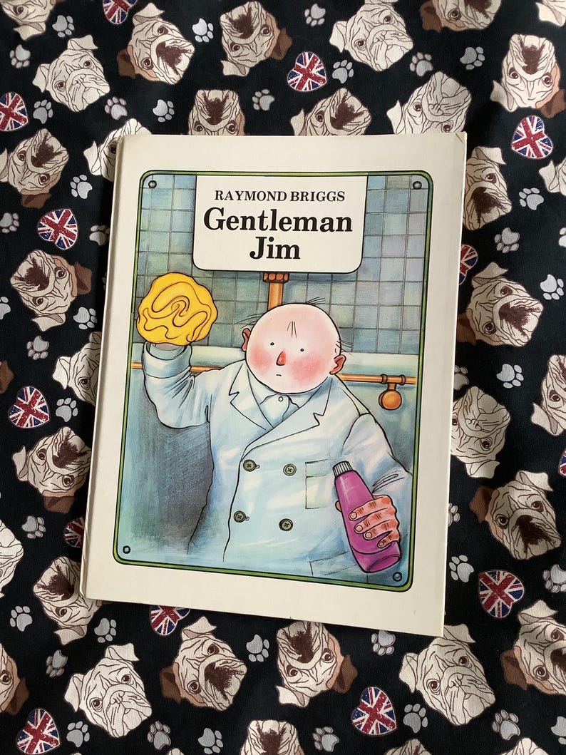 Puede incluir: Un libro titulado "Gentleman Jim" de Raymond Briggs. La portada muestra a un hombre con bata blanca con una esponja amarilla y una botella rosa. El libro est&aacute; sobre una tela negra con un estampado de pugs y banderas brit&aacute;nicas.