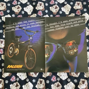 May include: A vintage Raleigh Grifter bicycle advertisement poster featuring a black bicycle with orange tires against a blue brick wall. The text reads: I'd seen the light. Nothing was going to come between me and my own Grifter. I thought I'd seen everything but then this black and gold number flashed past my eyes.