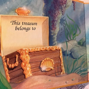 Pu&ograve; includere: Uno scrigno di legno aperto con finiture dorate e un design a conchiglia. Lo scrigno &egrave; seduto su un fondale sabbioso con alghe marine e altre forme di vita marina sullo sfondo. Il testo "Questo tesoro appartiene a" &egrave; scritto all'interno dello scrigno.