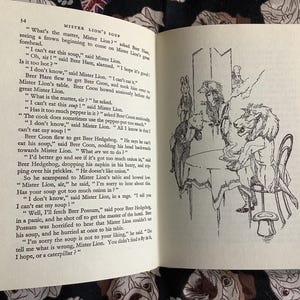 May include: An open book with a black and white illustration of a lion-headed character seated at a table with other animal figures. The text on the page reads "Mister Lion's Soup."