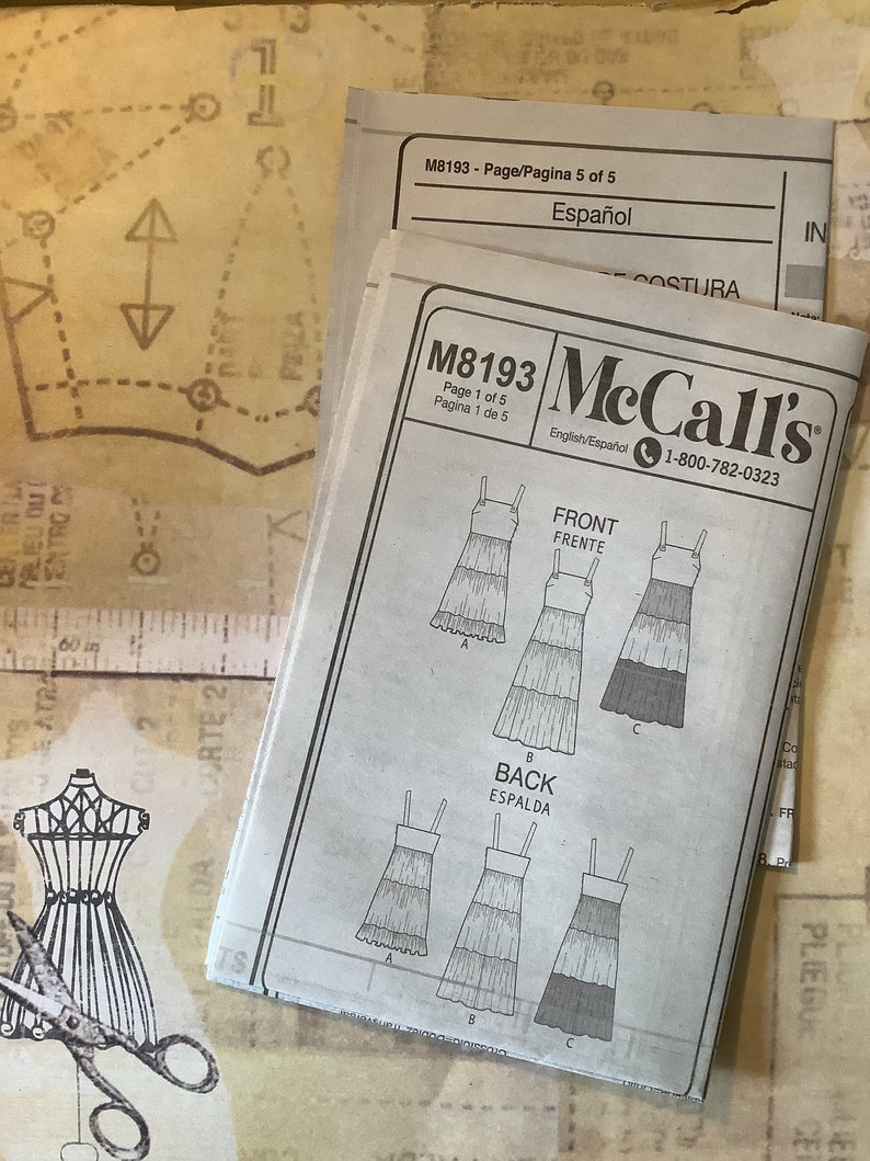 May include: A sewing pattern for a tiered dress with a sleeveless design. The pattern is for McCall's pattern number M8193 and is available in English and Spanish. The pattern includes instructions for both the front and back of the dress.