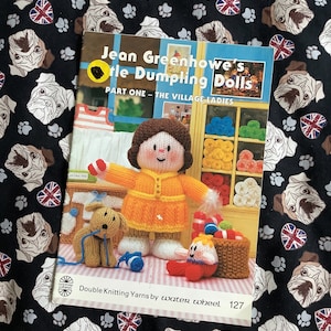 May include: A book titled "Jean Greenhowe's Little Dumpling Dolls" with a yellow and orange doll on the cover. The book is about knitting dolls and the cover says "Part One - The Village Ladies". The book also says "Double Knitting Yarns by water wheel 127".